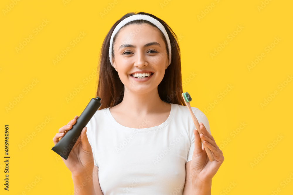 Beautiful young woman with activated charcoal tooth paste and brush on yellow background