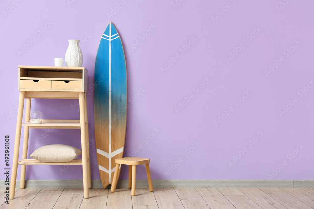 Surfboard, table and stool near color wall