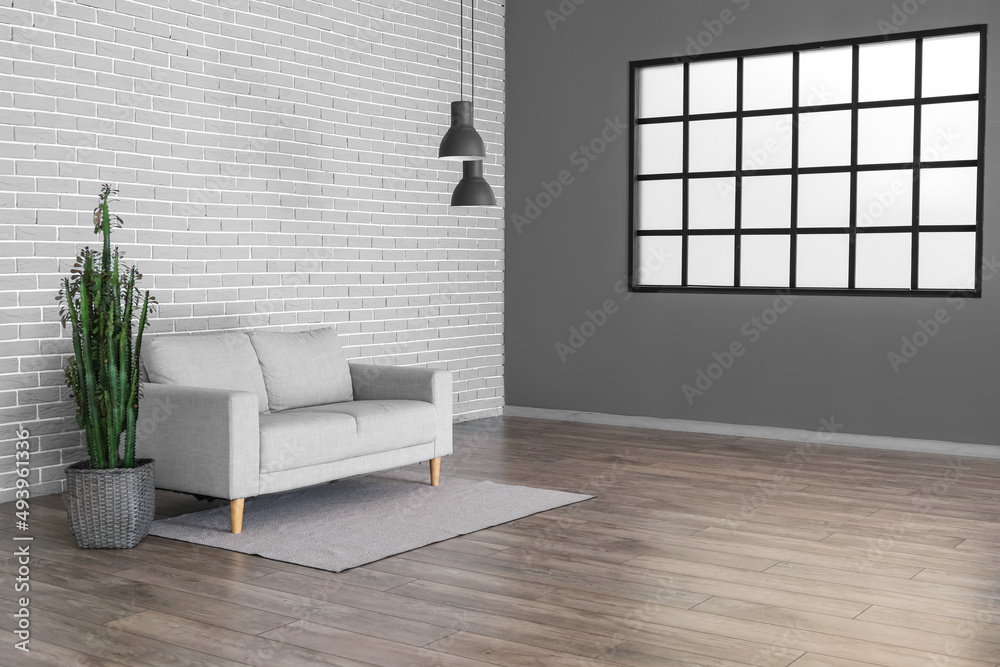 Modern sofa and cactus near grey brick wall in big room