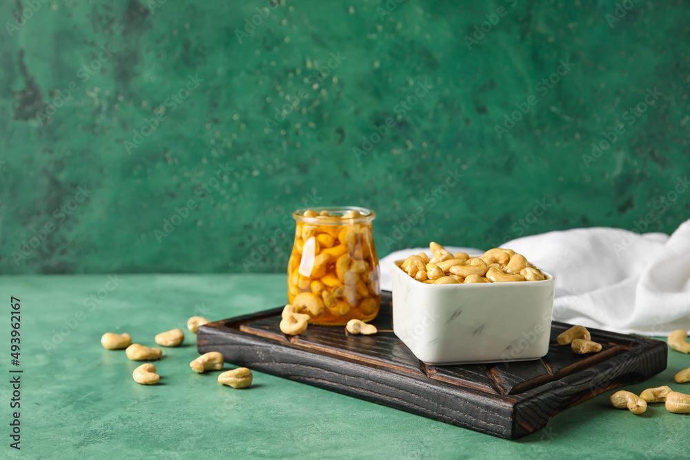 Board with sweet cashew nuts in honey on color background