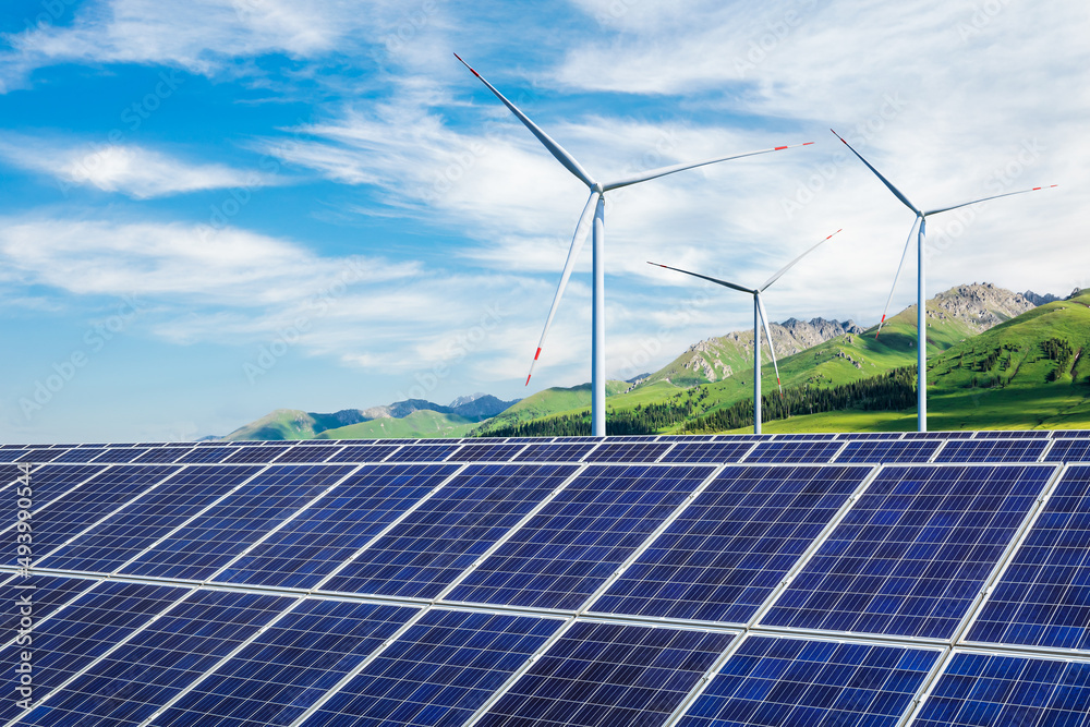 Solar panels and wind turbines with mountain landscape under blue sky. Green energy concept.