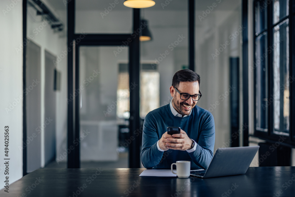 Portrait of a businessman, holding a mobile phone while looking at the laptop.