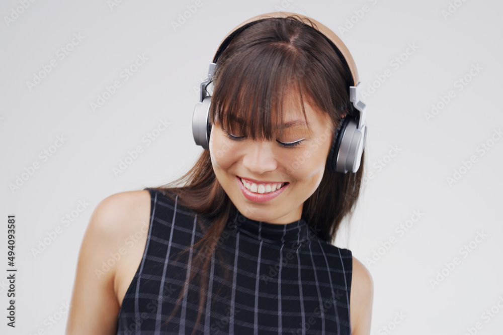 Letting the music do its thing. Studio shot of an attractive young woman dancing against a grey back