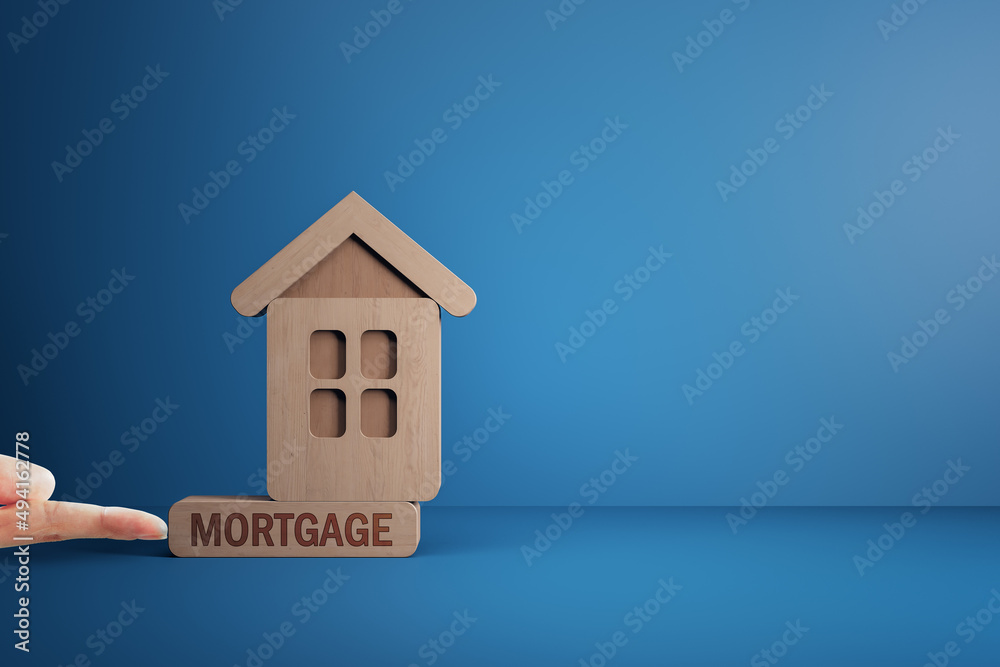 Finger pushing abstract wooden house on blue mortgage background with mock up place. Loan, bank and 