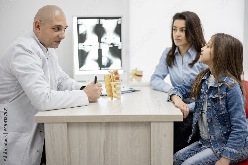 Pediatric orthopedist talking with a little girl and her mom during medical appointment at the offic