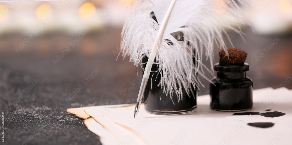 Feather pen, paper sheet and inkwells on table