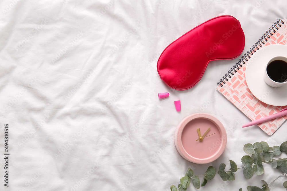 Sleep mask, alarm clock and cup of coffee on light fabric background