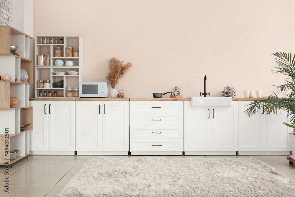 Interior of stylish kitchen with white counters, shelves and microwave oven