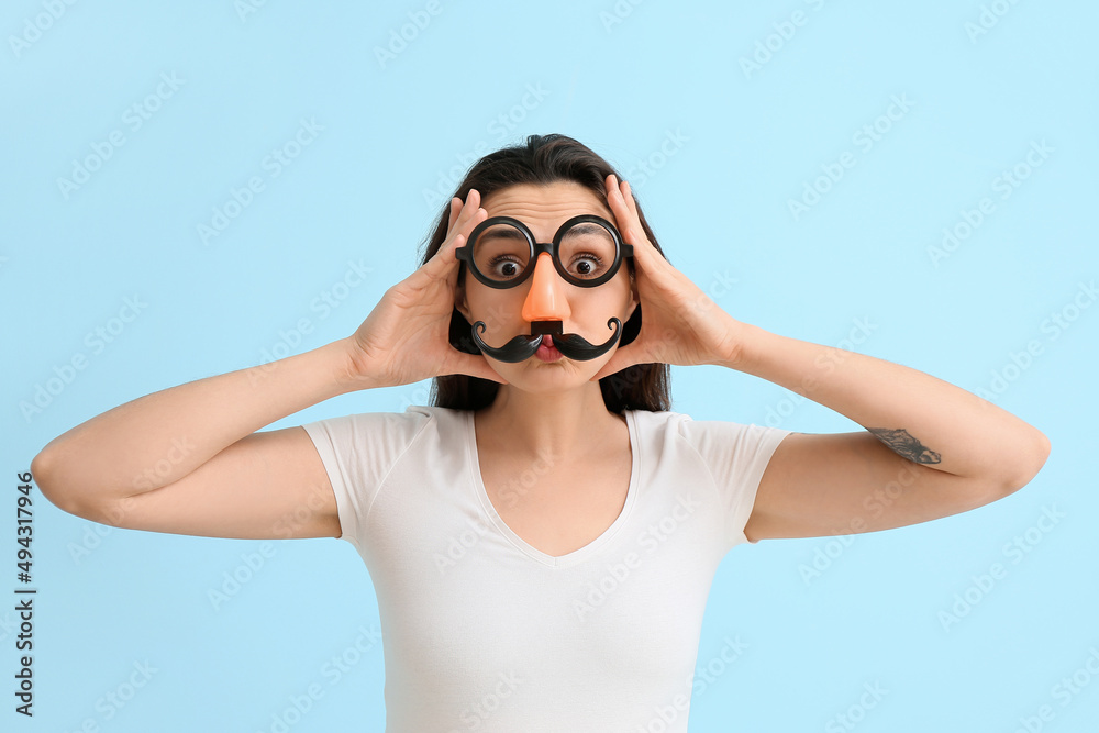 Young woman in funny disguise on blue background. April fools day celebration