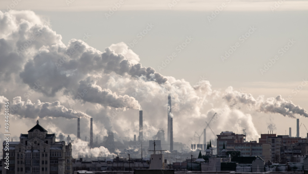 Chimneys smoke in winter against the background of the city and the sky.