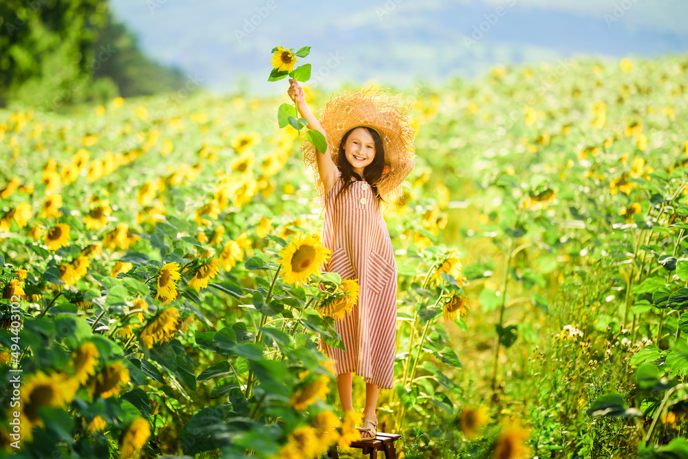 Hello sunny summer concept. Little girl has fan among blooming sunflowers field in summer.Full-lengt