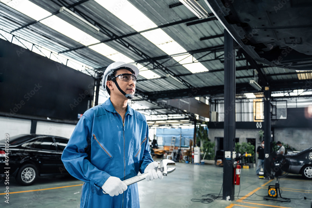 Asian automotive mechanic repairman look under car condition in garage