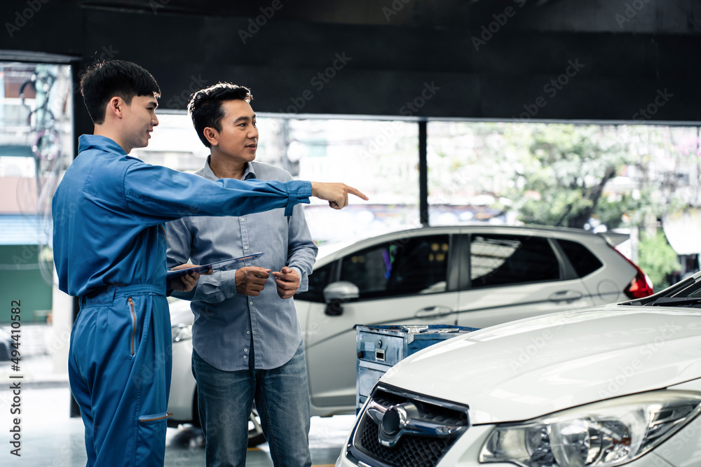 Asian automotive mechanic explain car condition to client in garage. 