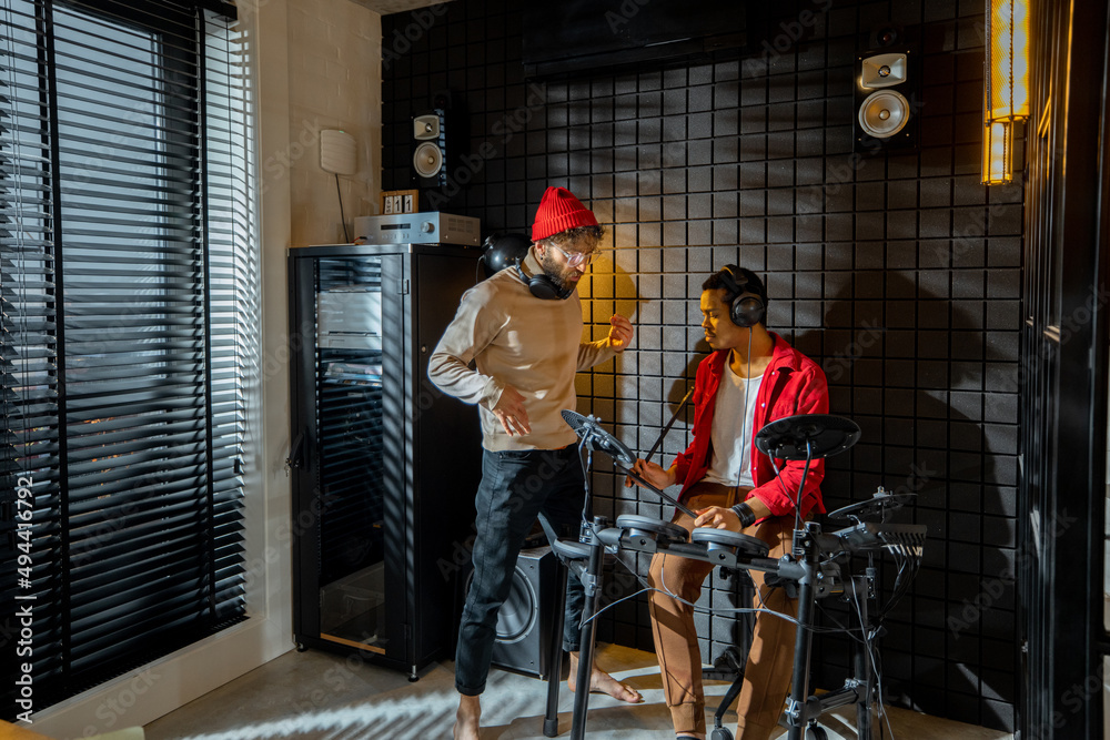 Two stylish men playing electric drums at small recording studio. Interior view on home studio. Cauc