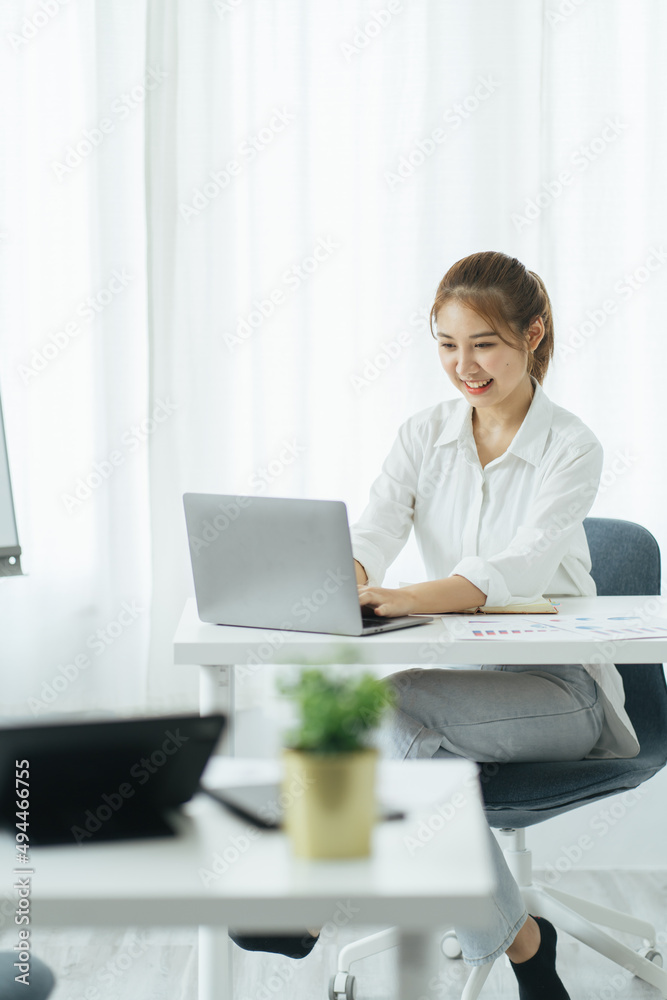 快乐的年轻亚洲女商人坐在办公室的工作场所。在lapto工作的年轻女性