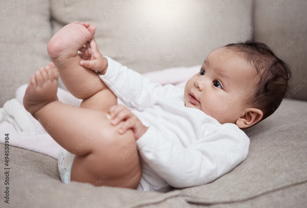 Hes just curious about everything. Shot of an adorable baby lying on a couch at home.