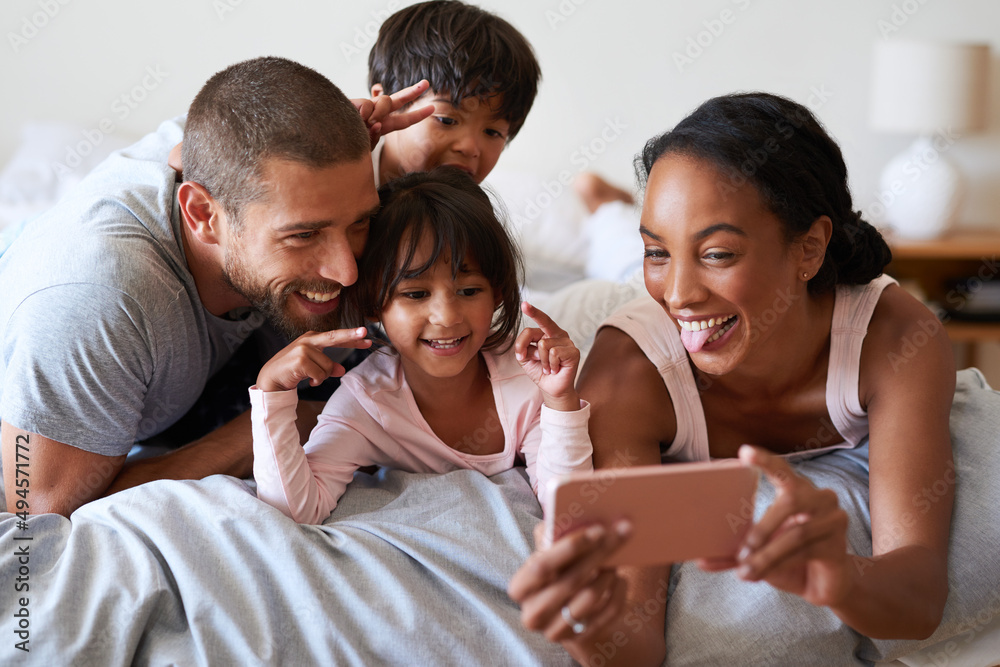 Smile for the camera. Shot of a beautiful young family of four taking a selfie with a cellphone in t