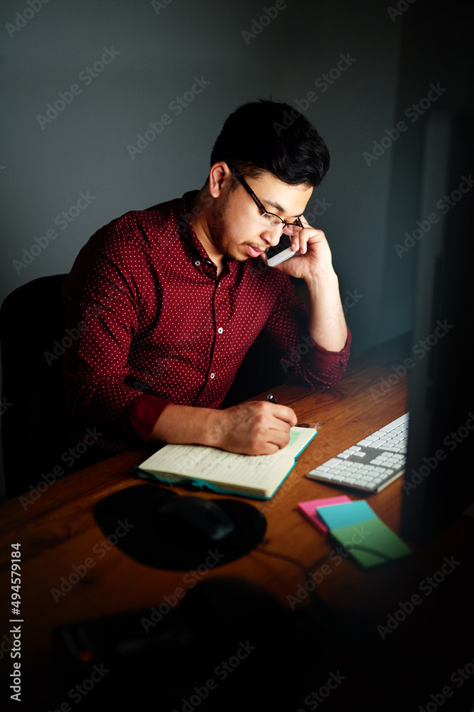 加班。一个年轻的男设计师在电话里聊天并做笔记的镜头