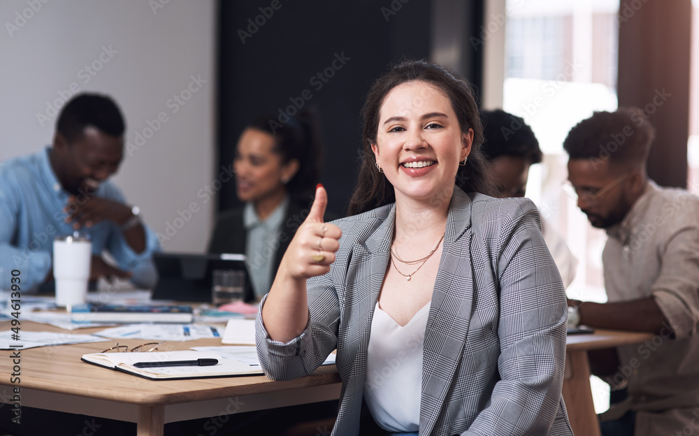 Business is all good. Portrait of a young businesswoman showing thumbs up in an office with her coll