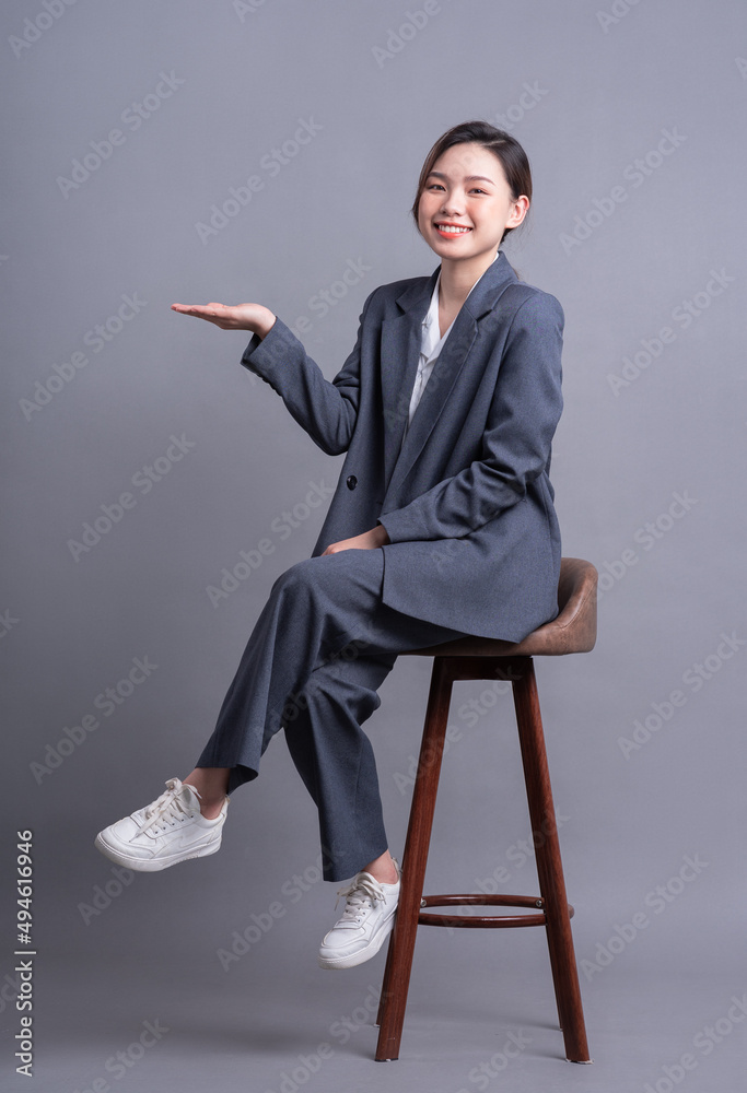 Young Asian businesswoman sitting on chair and posing on gray background