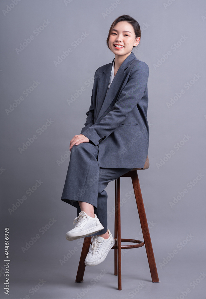 Young Asian businesswoman sitting on chair and posing on gray background