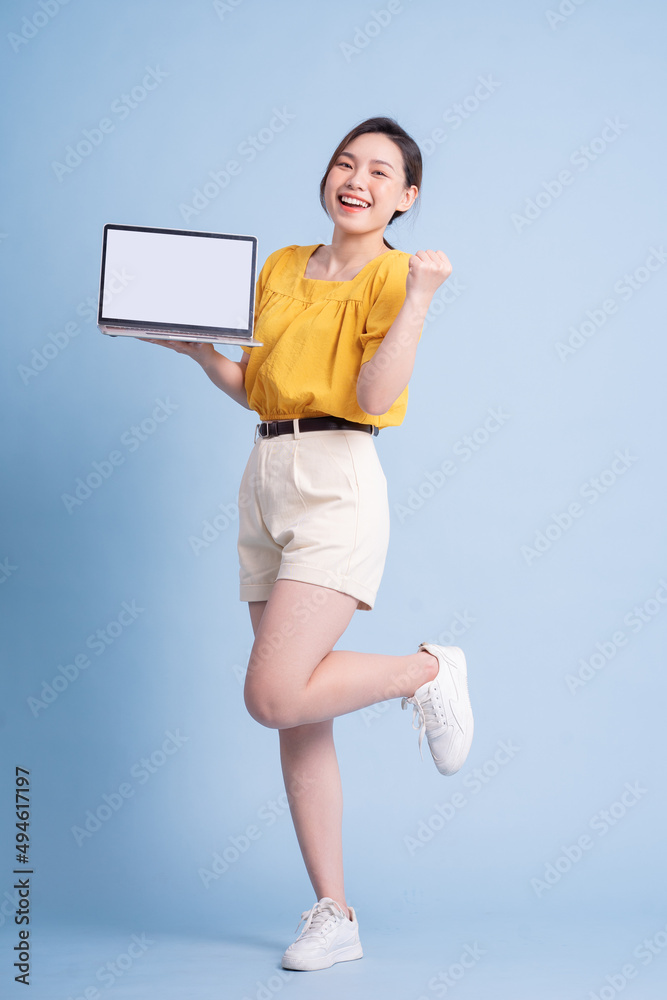 Full length image of young Asian girl using laptop on blue background