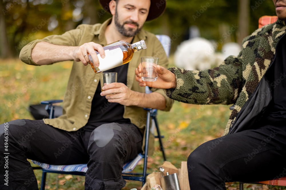 Caucasian man pour alcohol beverage to glass of latin male friend. Multiracial friends resting and f