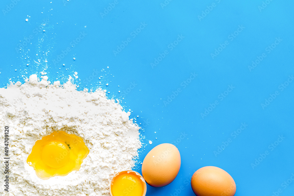 Baking background with eggs and flour on blue table. Top view.