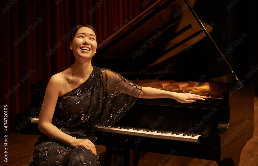 Proud of her performance. Shot of a young woman sitting by her piano at the end of a musical concert