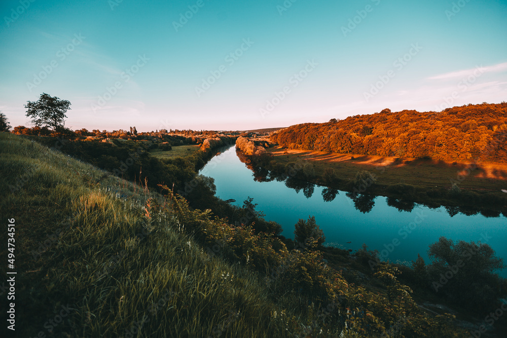 Picturesque landscape near the city with the sunset green grass and blue river