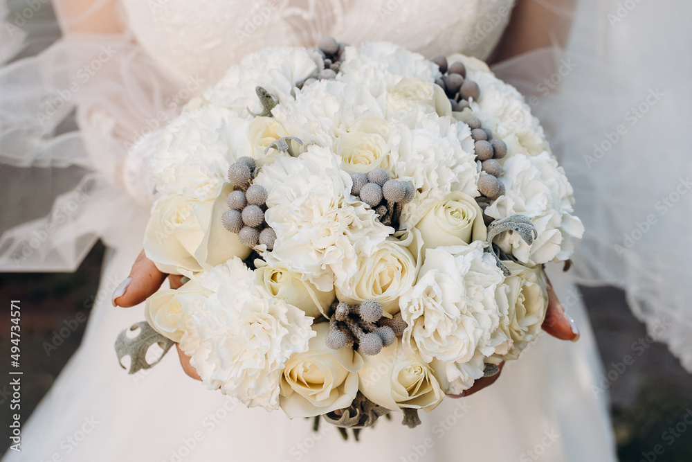 The bride holds a large luxury wedding bouquet of white roses on the front of the dress