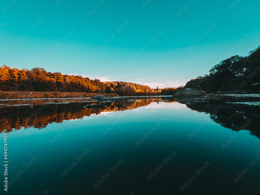 Sunset on the forest over the lake. Blue water and cool reflection of sky. The clean water