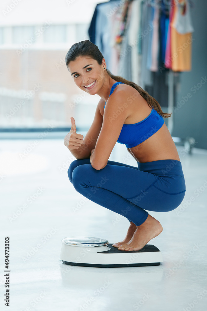 My weight loss goals are right on track. Portrait of a fit young woman weighing herself on a scale a