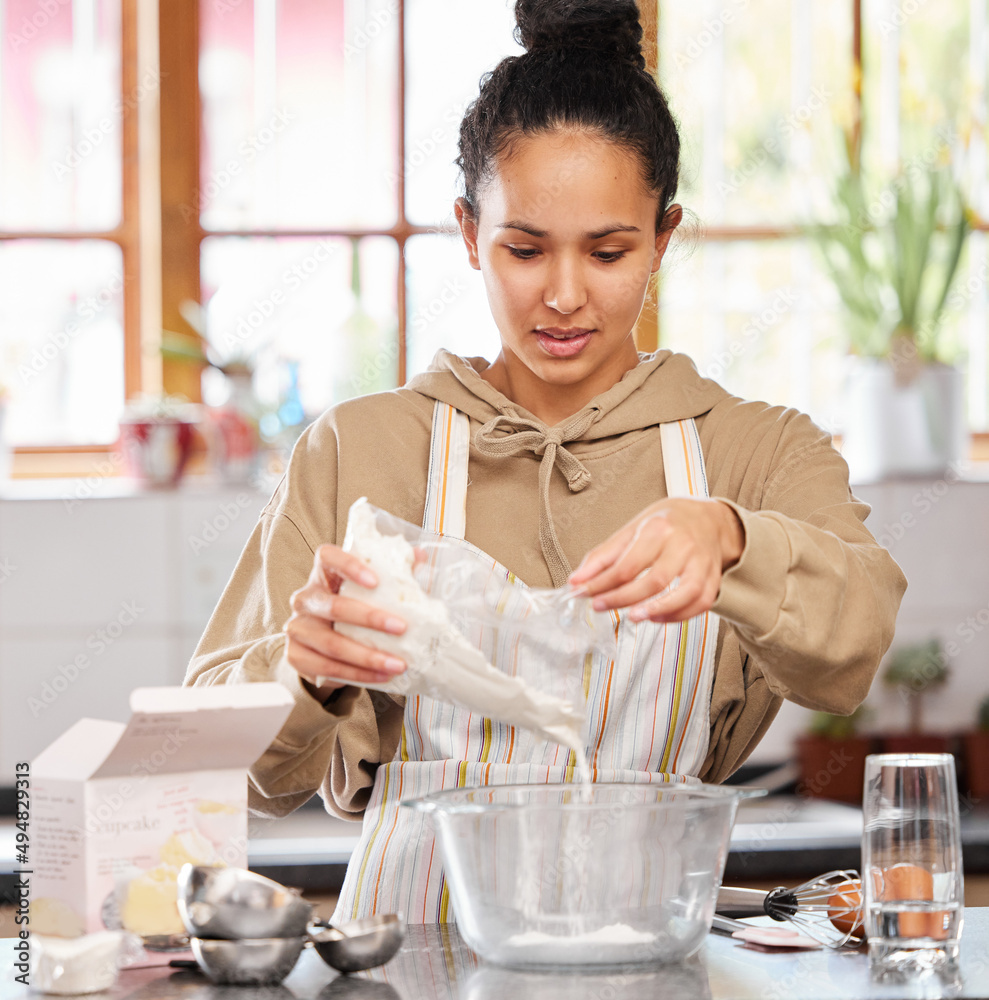 The home made stuff tastes the best. Shot of a young woman adding flour to a bowl while baking.