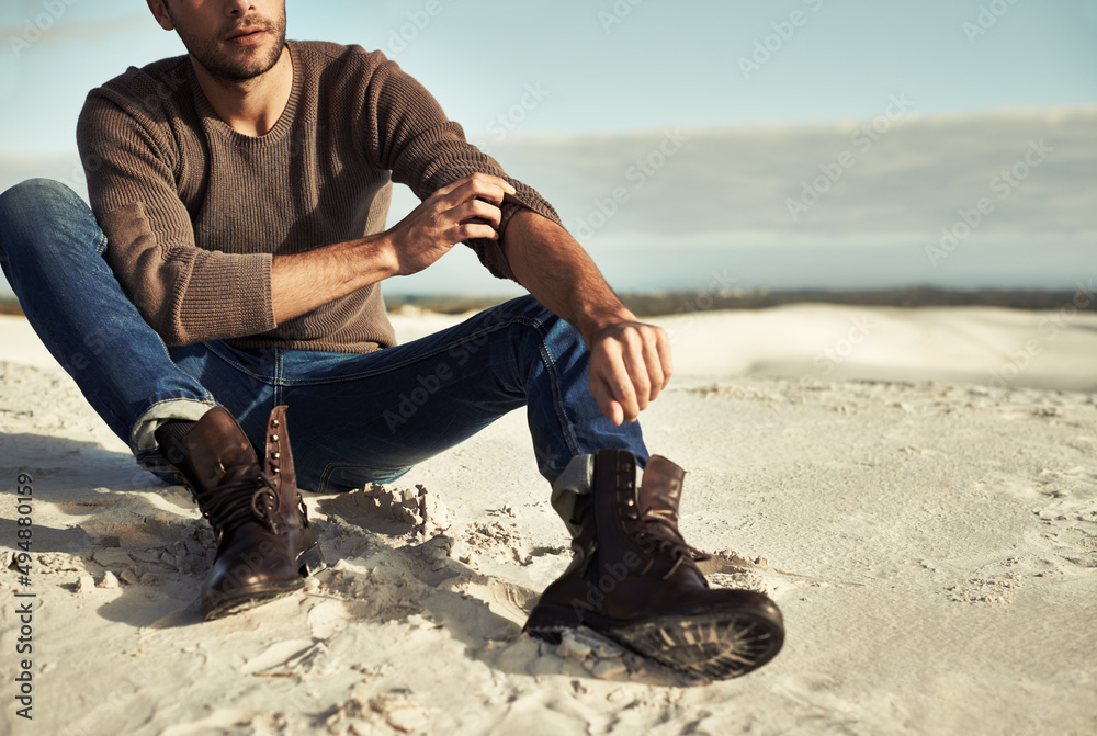 海边的时刻。一个穿着牛仔裤和靴子的男人坐在海滩上。