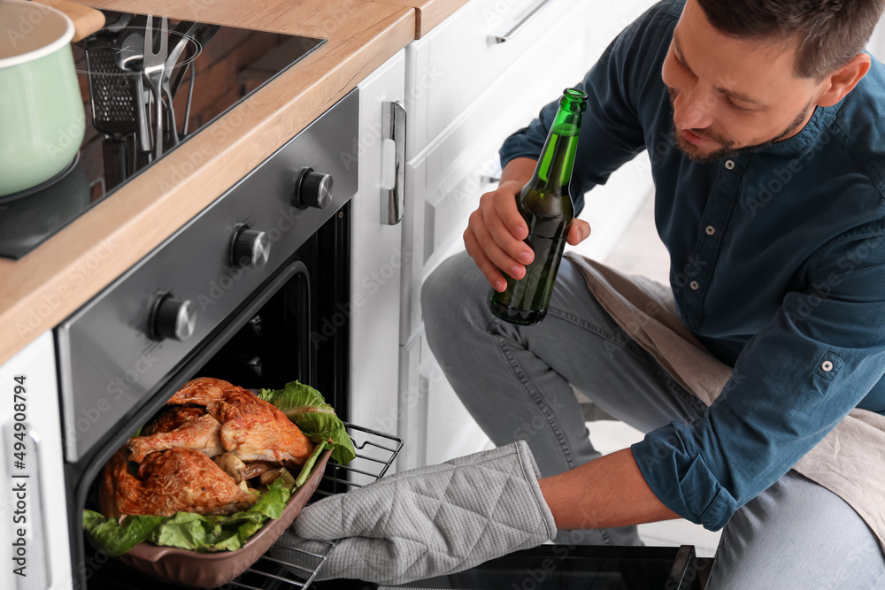 Handsome man drinking beer while cooking in kitchen