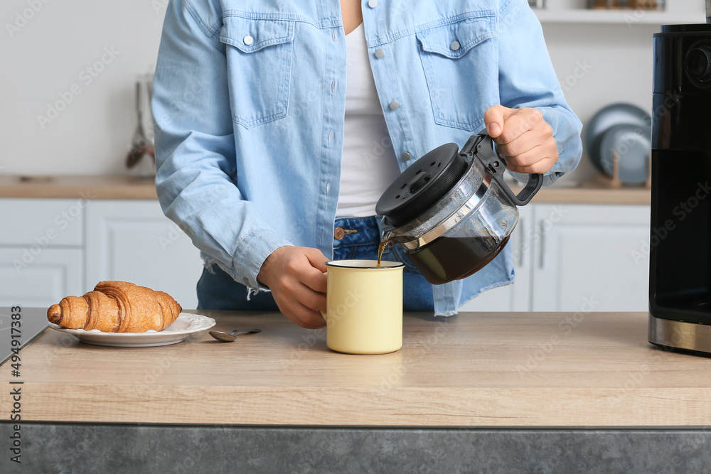 Young woman pouring hot coffee from pot in kitchen, closeup