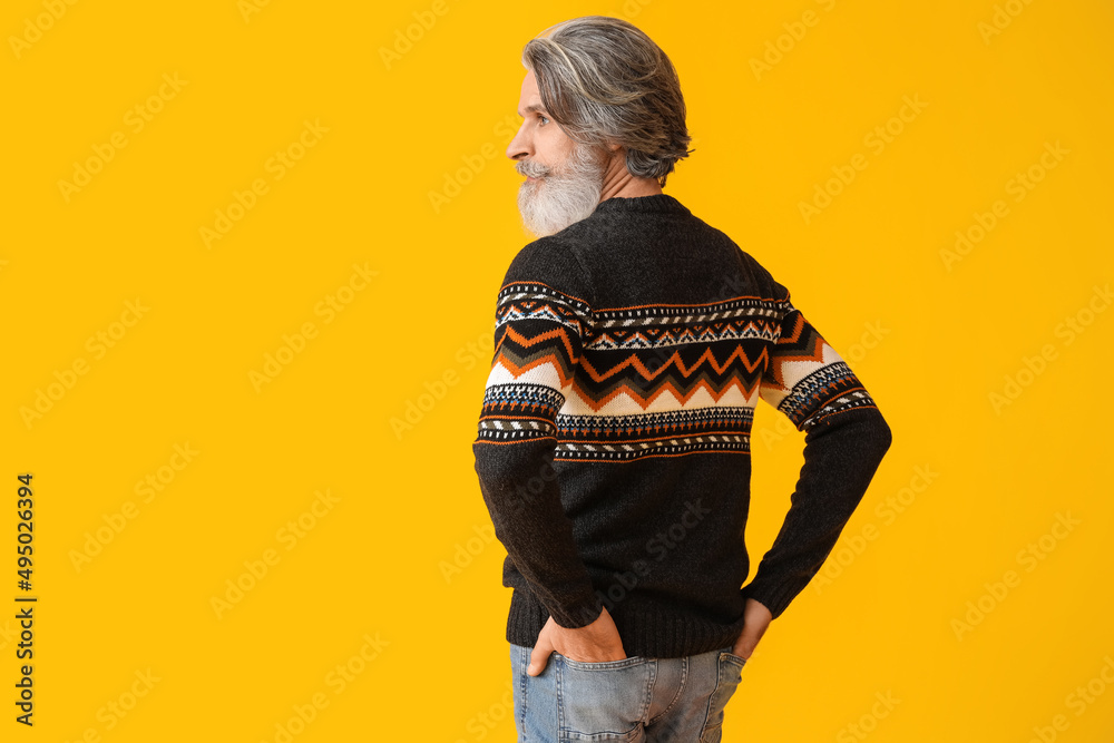 Handsome senior man in knitted sweater on yellow background