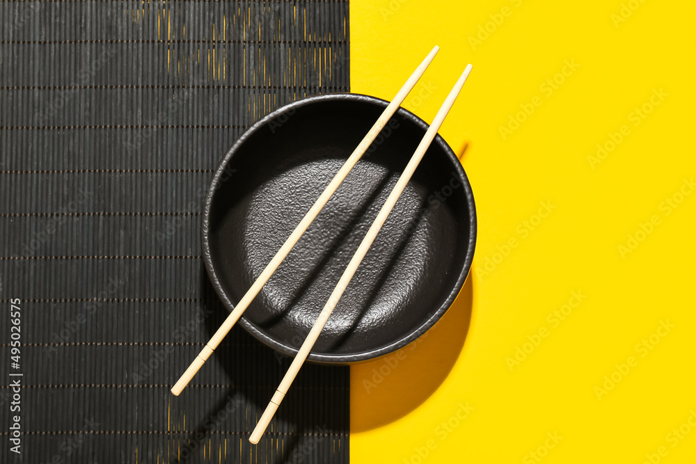 Bamboo mat with Chinese bowl and chopsticks on color background