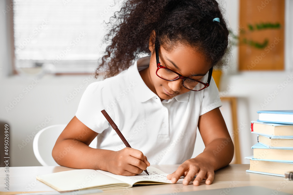 Little African-American girl writing in copybook while studying with online tutor at home