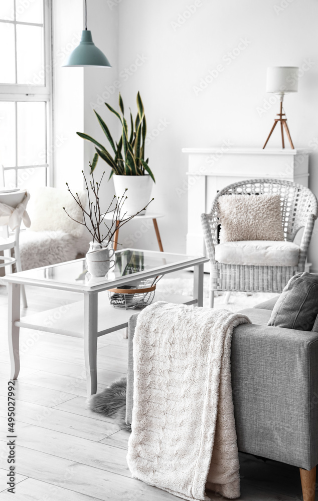 Vase with tree branches and cups on glass table in living room interior