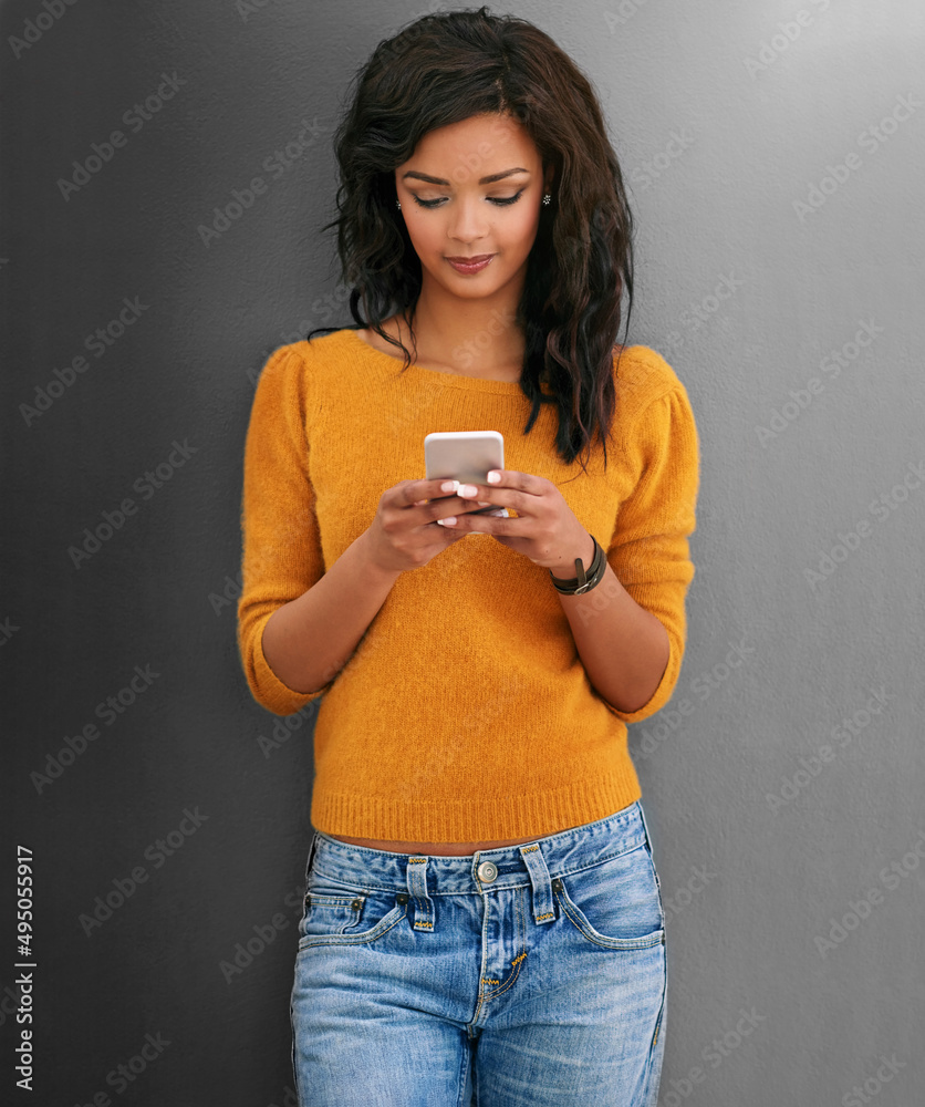 Staying in the social loop with modern technology. Studio shot of a young woman using her phone agai