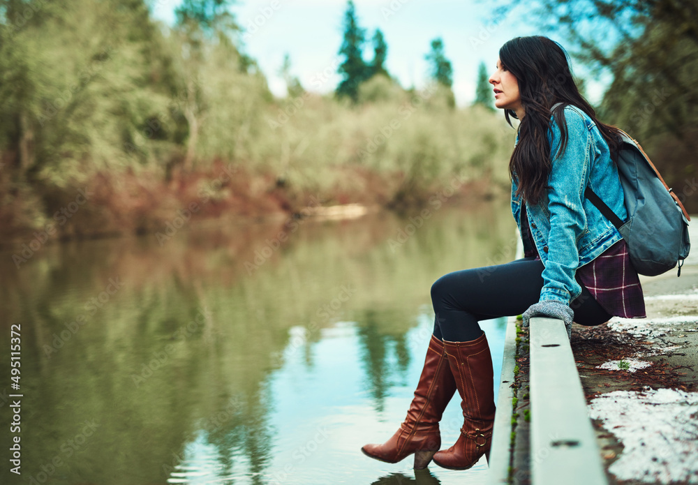 The water looks amazing. Shot of a young woman sitting by a lake outdoors.