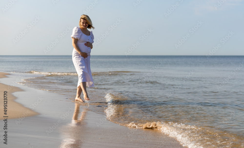 Pregnant beautiful woman walking barefoot on seashore