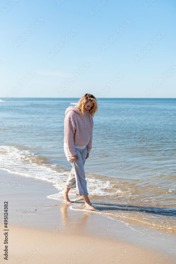 穿着亚麻长裤的女人赤脚在沙滩上行走