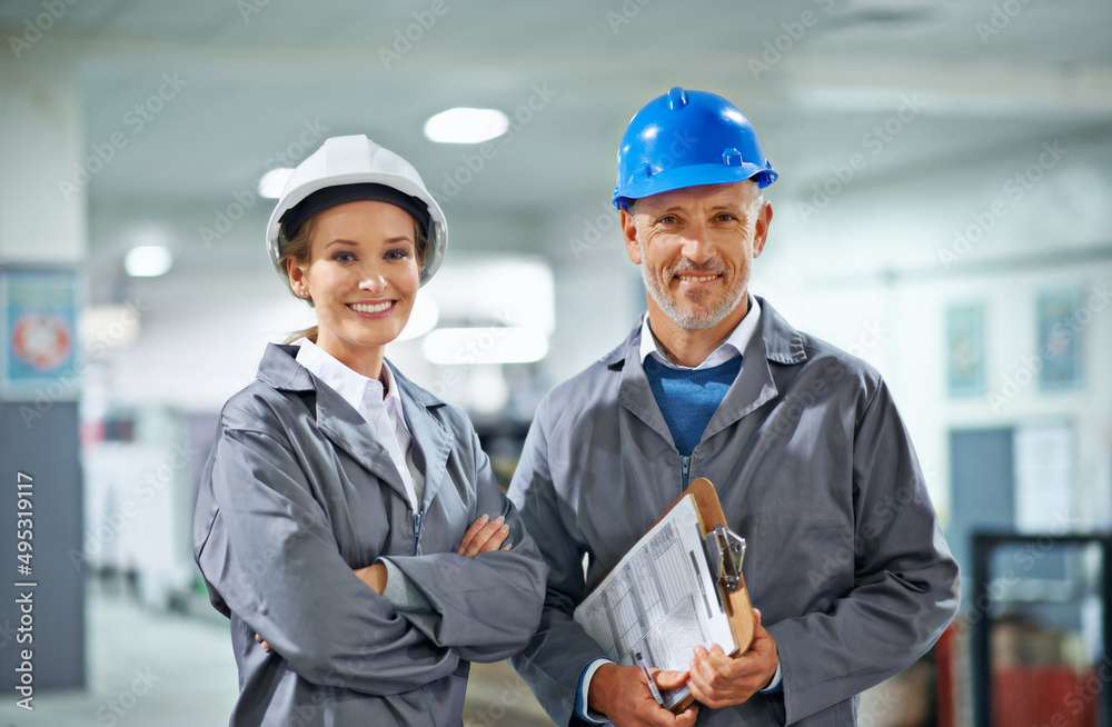 Happy in our profession. Two people wearing hardhats smiling at the camera in a factory.