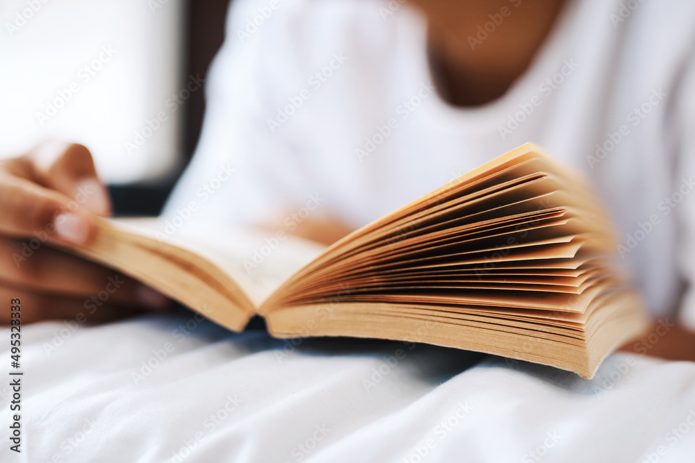 Stay home and get your read on. Cropped shot of a young man reading a book while lying on his bed.