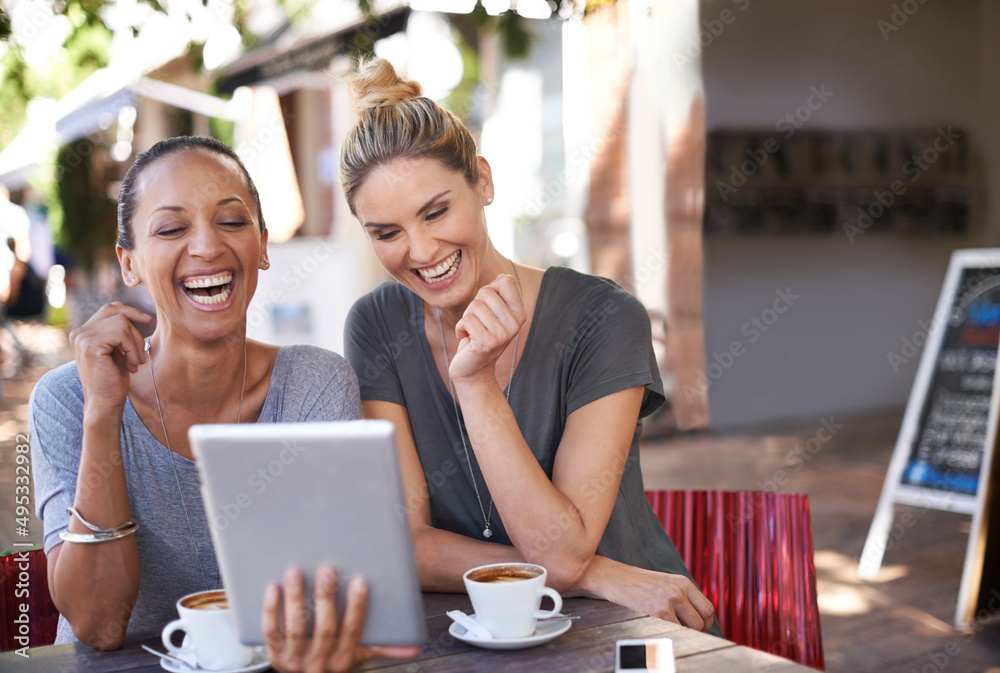 Sharing a laugh between besties. Two young women looking at a tablet in a coffee shop.