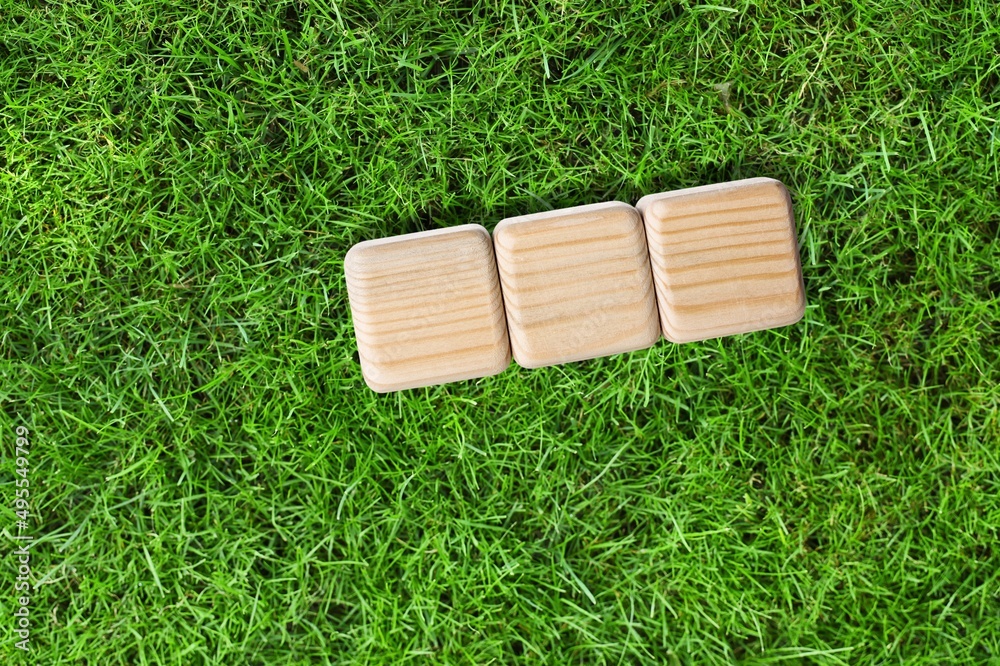 Three wooden cubes on green grass