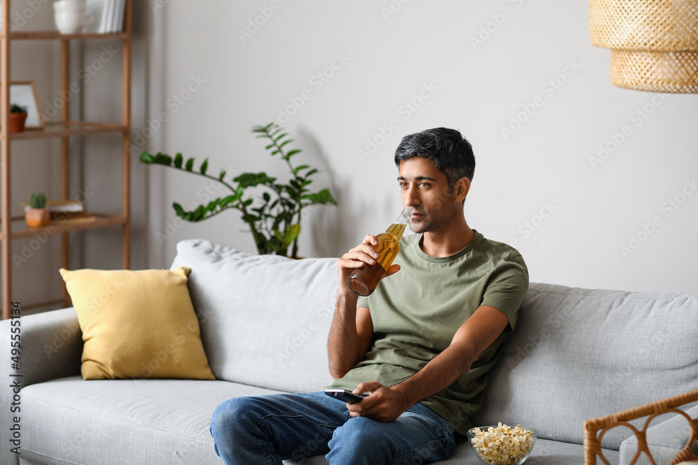 英俊男子在家看电视时喝啤酒